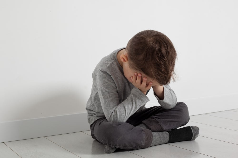 a depressed little boy sitting on the floor with his face in his hands